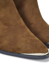 Bruine suède laarzen met een spitse neus, voorzien van een metalen zilveren accent op de neuskap en een donkere zool.