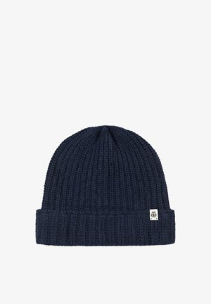 Navy blue knitted beanie with a folded brim and a small white tag featuring a black emblem on the cuff.
