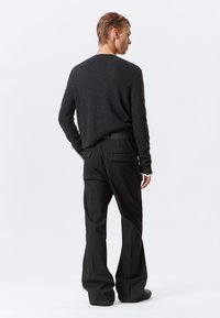 Szary dzianinowy sweter o luźnym kroju, w połączeniu z czarnymi spodniami w prążki, które mają tylne kieszenie i pasek. Całość charakteryzuje się gładką teksturą.