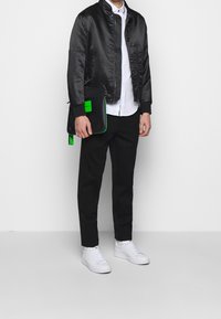 Svart satin bomberjacka, vit skjorta, svarta byxor och vita sneakers. Gröna accentdetaljer på väskan och jackans ärmar.