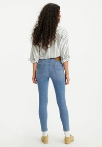 Jeans ajustados azules de cintura alta, hechos de denim. Presentan una etiqueta de cuero marrón, dos bolsillos traseros y un diseño ajustado.