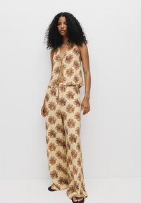 Losse, mouwloze top en brede broek in crème met een bruin bloemenpatroon. Zachte stof met een relaxte silhouet en een strikdetail.