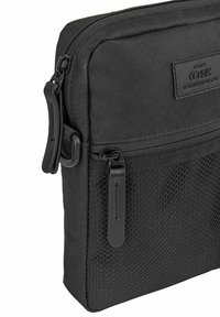 Czarna torba na ramię z tkaniny, z teksturowanym wzorem, zamykaną na zamek komorą oraz płaskim, prostokątnym kształtem i naszywką z logo.