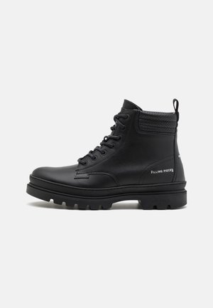 Bottine noire en cuir à lacets avec col perforé rembourré, semelle épaisse et logo "Filling Pieces" sur le côté.