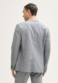 Grauer maßgeschneiderter Blazer von hinten betrachtet, mit einer glatten Textur, einem einzelnen Schlitz und geknöpften Manschetten. Der Stoff zeigt ein dezentes Muster.