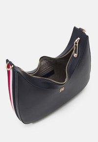 Marineblaue Lederhandtasche mit geschwungener Form, die einen goldenen Reißverschluss und eine strukturierte Oberfläche aufweist. Das Innere ist mit einem weichen Material ausgekleidet. Akzentuiert mit roten und weißen Streifen.