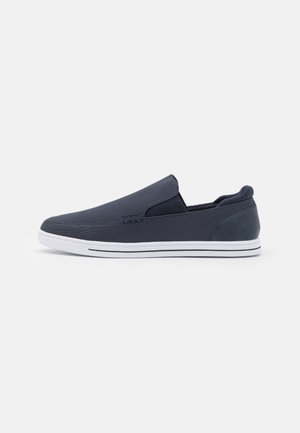 Chaussure décontractée pour homme à enfiler, en tissu gris foncé avec semelle en caoutchouc blanche et détail de couture minimaliste, vue de côté sur fond blanc.