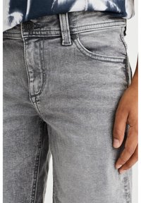 Jeans de mezclilla gris con una textura desgastada, que presentan un diseño de cinco bolsillos, cierre de botón metálico y detalles de costura visibles.