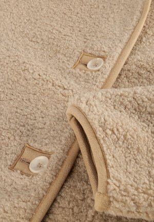 Beige fleece stof met een zachte, gestructureerde afwerking, voorzien van een tan rand en knopenaccenten nabij de gestikte zakken.