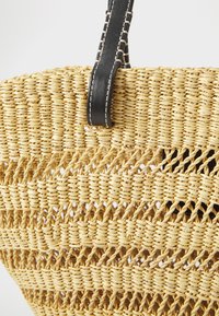 Kudottu olkikori, jossa on kerroksittain muotoilu, luonnollinen beige väri ja musta nahkahandles valkoisine ompeleineen.