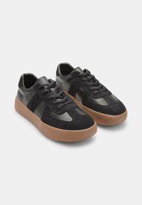 Svarta sneakers med en kombination av slätt läder och mocka, med en rundad tan-färgad gummisula och traditionell snörning.