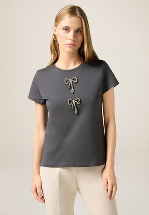 Graues T-Shirt aus Baumwolle mit zwei dekorativen Schleifen mit schimmernden Akzenten in der Mitte. Kurze Ärmel und eine lockere Passform.