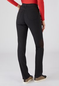 Jeans negros de pierna recta con cinco bolsillos, cintura alta y una textura suave, combinados con zapatillas de diseño.