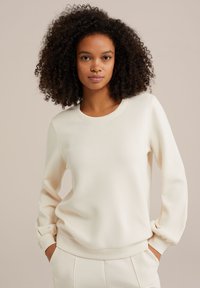 Krémový sveter s okrúhlym výstrihom a zberanými manžetami. Tkanina vyzerá mäkká a hladká; má voľný strih a minimalistický dizajn.
