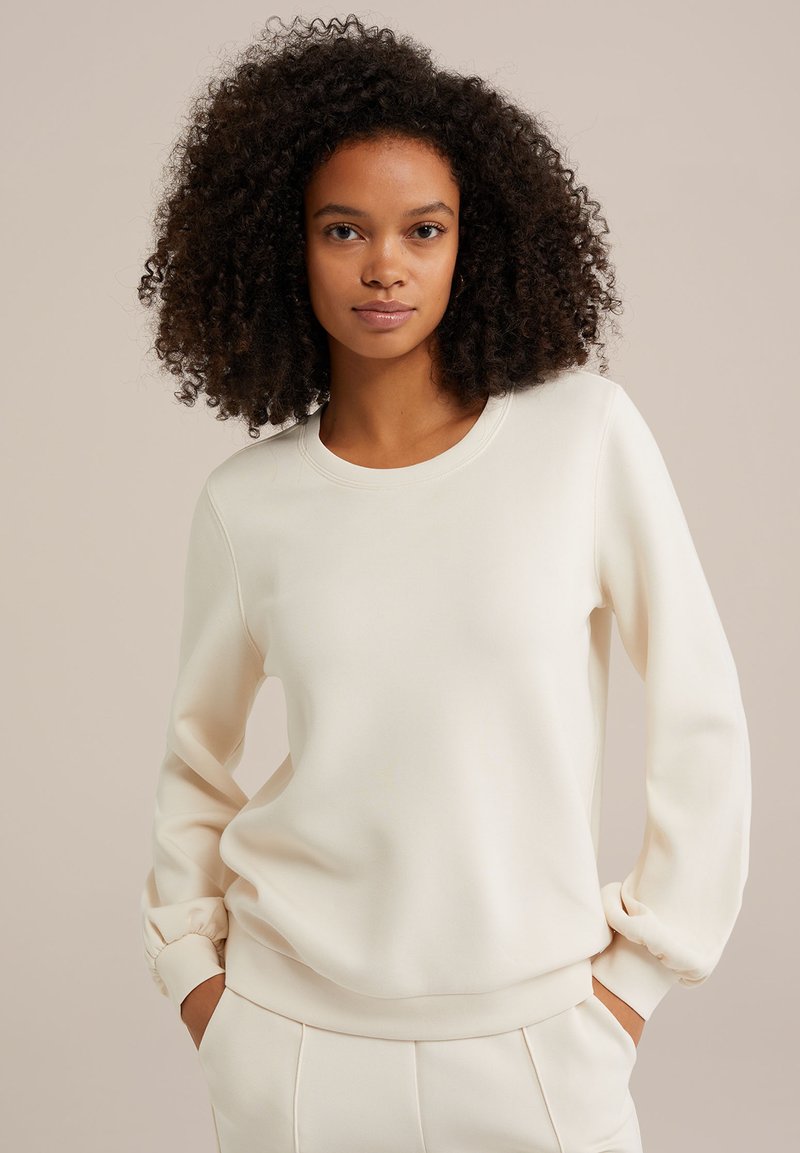 Krémový sveter s okrúhlym výstrihom a zberanými manžetami. Tkanina vyzerá mäkká a hladká; má voľný strih a minimalistický dizajn.