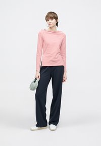 Długi rękaw w paski w kolorze czerwonym i białym, zestawiony z luźnymi granatowymi spodniami i białymi trampkami. Modelka trzyma jasnzię zieloną torbę.