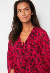 Blusa floreale rossa con motivi botanici neri, scollo a V, dettaglio con laccio nella parte anteriore, materiale trasparente, maniche svolazzanti e vestibilità comoda.
