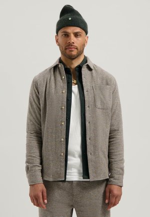 Gecar toneerde geblokte overhemden in tan en bruin, met een zakje, gedragen over een wit T-shirt, gecombineerd met bijpassende broek en een groene beanie.