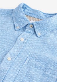 Helehall sinine nööbitav särk tekstuurse mustriga, millel on krae, valged nupud ja rinnatasku. Tekstuuriga kangas visuaalse huvi tekitamiseks.