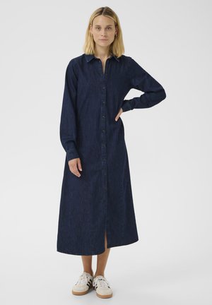 Denim shirt dress in dark blue, featuring a button-down front, long sleeves, and a mid-length design. Paired with white sneakers.