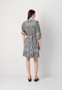 Monivärinen mekko, jossa on geometrisia kuvioita tummansinisessä, valkoisessa ja keltaisessa. Mekko on rento malli, lyhyet hihat ja vyötäröllä solmittava yksityiskohta.