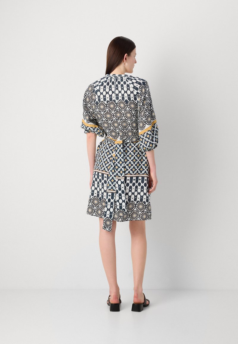 Bunt gemustertes Kleid mit geometrischen Mustern in Marineblau, Weiß und Gelb. Es hat eine lockere Passform, kurze Ärmel und eine gewickelte Taillendetails.