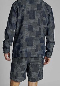 Marinblå tvådelad outfit bestående av en långärmad skjorta och shorts, båda med ett texturerat geometriskt mönster. Materialet verkar vara lätt och andningsbart.