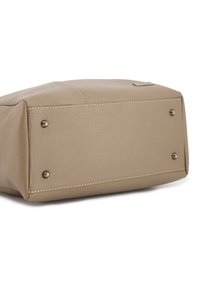 Leichtbeige Lederhandtaschenunterseite mit gesteppten Details, flache rechteckige Form und vier Metallfüße für Stabilität. Kleines, gebrandetes Metallschild vorhanden.