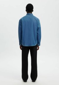 Jeansskjorta i gradient blåtoner, långa ärmar, knäppta manschetter, rak skärning, i kombination med svarta vida byxor. Enkla kragsdesign.