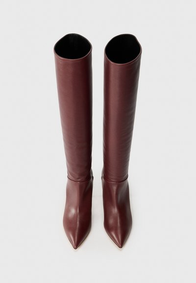 Bottes en cuir bordeaux montantes avec une texture lisse, bout pointu et un design long et ajusté. Style minimaliste sans quincaillerie visible.