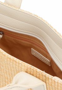 Sac tote en paille tissée avec des accents en cuir synthétique crème, présentant une poche intérieure zippée et une finition lisse et texturée.