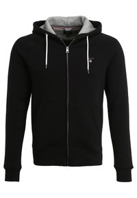 Felpa nera con zip e cappuccio foderato in grigio, dotata di lacci bianchi, tasche laterali e un piccolo logo sul petto. Tessuto liscio.