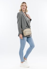 Borsa a tracolla beige con texture in pelle liscia e accessori in argento, dotata di scomparto con zip e tracolla regolabile.