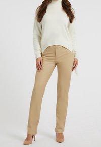Beżowe, dopasowane spodnie o gładkiej fakturze, zestawione z luźnym kremowym sweterkiem z wysokim kołnierzem i ściągaczami przy mankietach.