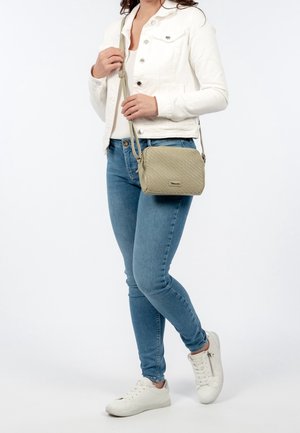 Jasnozielona torebka na ramię o teksturowanym, plecionym wzorze, prostokątnym kształcie i regulowanym pasku, zestawiona z białą kurtką i niebieskimi dżinsami.