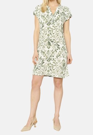 Kvinde iført en kortærmet, knælængde kjole med grønt og beige blomsterprint samt beige slingback sko med lav hæl.