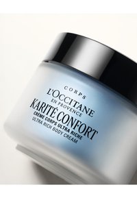 L'Occitane ultra bogaty krem do ciała w okrągłym szklanym słoiku z gradientowym wykończeniem od niebieskiego do białego, wyposażony w czarną pokrywkę i wyraźną etykietę z czarnym napisem.