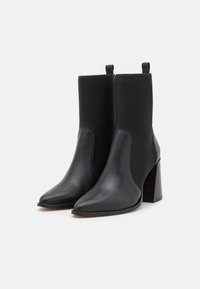 Botas negras hasta el tobillo con un elegante exterior de cuero, parte superior de punto acanalado, puntera afilada y un tacón grueso. Dos lengüetas para ponerlas y quitarlas fácilmente.