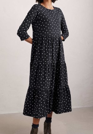 Frau trägt ein schwarzes Midi-Kleid mit weißen Polka-Dots und dreiviertellangen Ärmeln, kombiniert mit dunklen Socken und Schnürstiefeln.