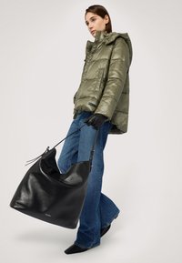 Puffjacka i olivgrön med huva, kombinerad med utsvängda blå jeans. Modellen håller en stor svart läderhandväska med axelrem.