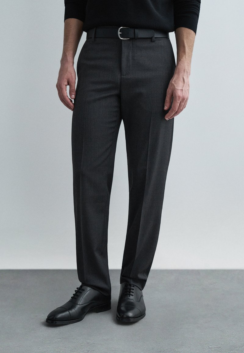 Gray tailored trousers with a subtle texture, featuring a flat front, and paired with black leather shoes and a black belt.