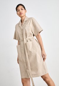 Stripete beige skjortekjole med korte ermer, knappeløsning, belte i midjen og to frontlommer. Glatt, lett stoff.