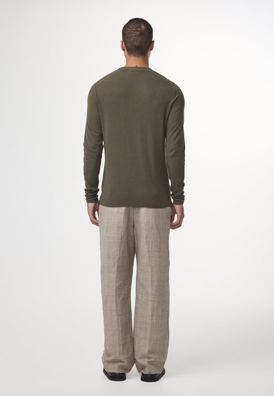 Una camicia a maniche lunghe verde oliva abbinata a pantaloni larghi beige a scacchi, con una texture morbida e una vestibilità rilassata. Le scarpe nere completano il look.
