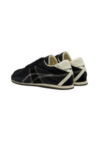 Zapatillas negras con acentos blancos, que cuentan con un forro suave, costuras en contraste y un diseño aerodinámico para un aspecto moderno.