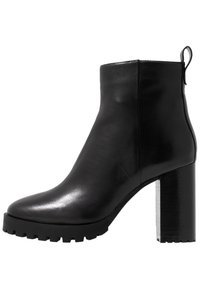 Musta nahkasaapas nilkkapituudella, jossa on sileä pinta, tukeva kumipohja ja korkea tukipohja. Takana on vetovaljaat, jotka helpottavat pukemista.