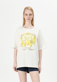 T-shirt oversized blanc avec un graphique de citron et le texte "LES CITRONS" et "Limonade Frais et Naturel." Manches courtes, en coton doux.