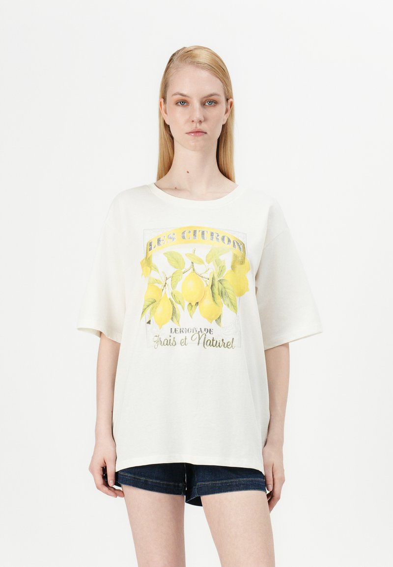 T-shirt oversized blanc avec un graphique de citron et le texte "LES CITRONS" et "Limonade Frais et Naturel." Manches courtes, en coton doux.