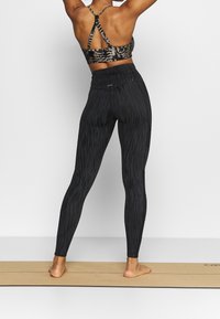 Czarne legginsy z fakturowanym wzorem, wysokim stanem i dopasowanym krojem, połączone z pasującym sportowym biustonoszem w zwierzęcy print.