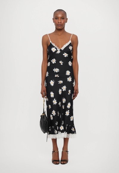 Robe midi noire à fleurs avec des marguerites blanches, bordure en dentelle à l'ourlet, fines bretelles réglables et silhouette ajustée. Portée avec un sac noir.