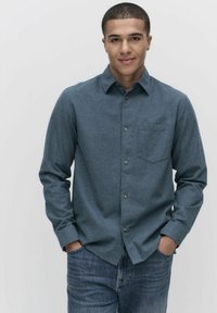 Donkerblauw overhemd met knopen, gemaakt van textuurstof, met een borstzak en bruine knopen, gecombineerd met denim jeans.